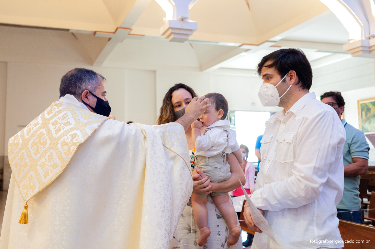 Imagem do padre batizando a criança no colo da mãe na Paróquia São Francisco de Paula na Barra da Tijuca no Rio de Janeiro
