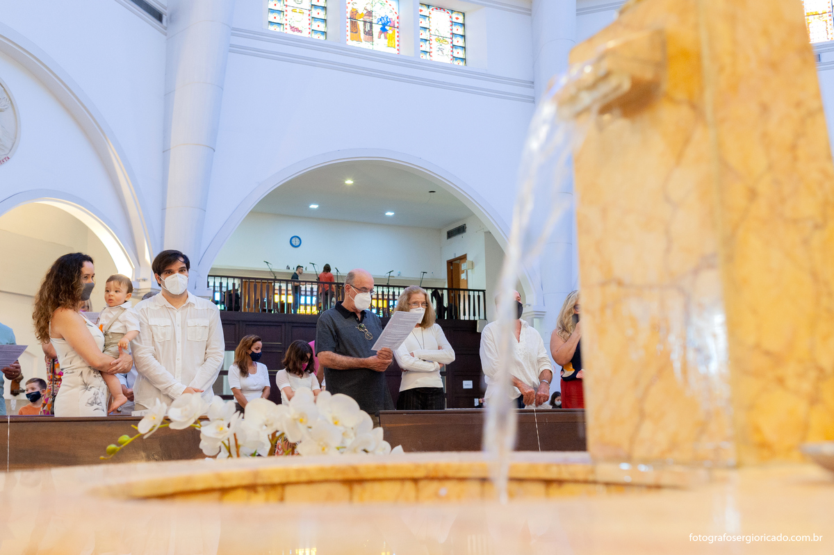 Fotografia dos pais esperando para batizar o filho na fonte batismal na Paróquia São Francisco de Paula na Barra da Tijuca no Rio de Janeiro