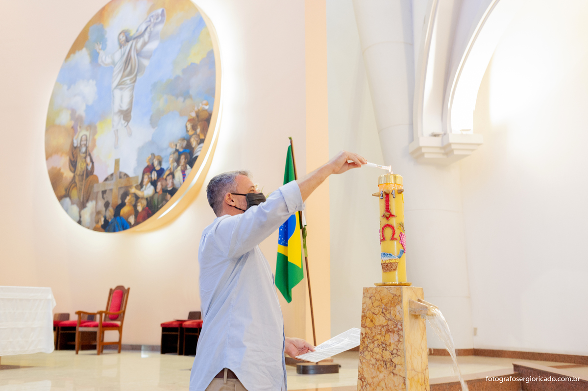 Imagem do padrinho acendendo a vela do círio pascal durante batizado na Paróquia São Francisco de Paula na Barra da Tijuca no Rio de Janeiro   
