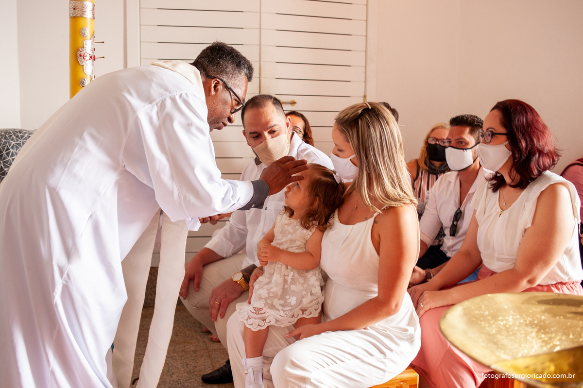 Fotografia dos pais com criança recebendo o batismo na Capela de Nossa Senhora Aparecida no Cristo Redentor localizado no Morro do Corcovado no Rio de Janeiro