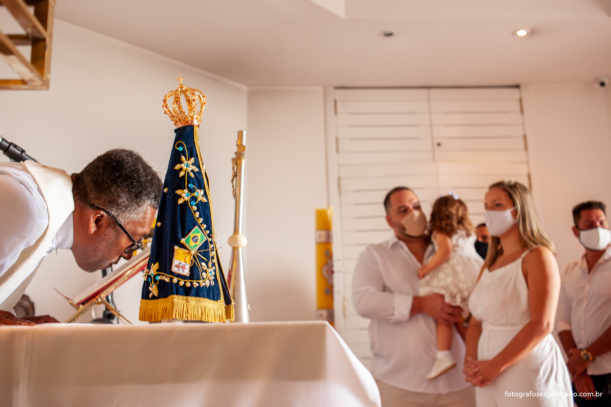 Foto dos pais com o padre realizando cerimônia de batismo na Capela de Nossa Senhora Aparecida no Cristo Redentor localizado no Morro do Corcovado no Rio de Janeiro