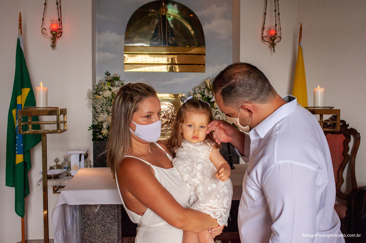 Fotografia dos pais com criança na cerimônia de batismo na Capela de Nossa Senhora Aparecida no Cristo Redentor localizado no Morro do Corcovado no Rio de Janeiro