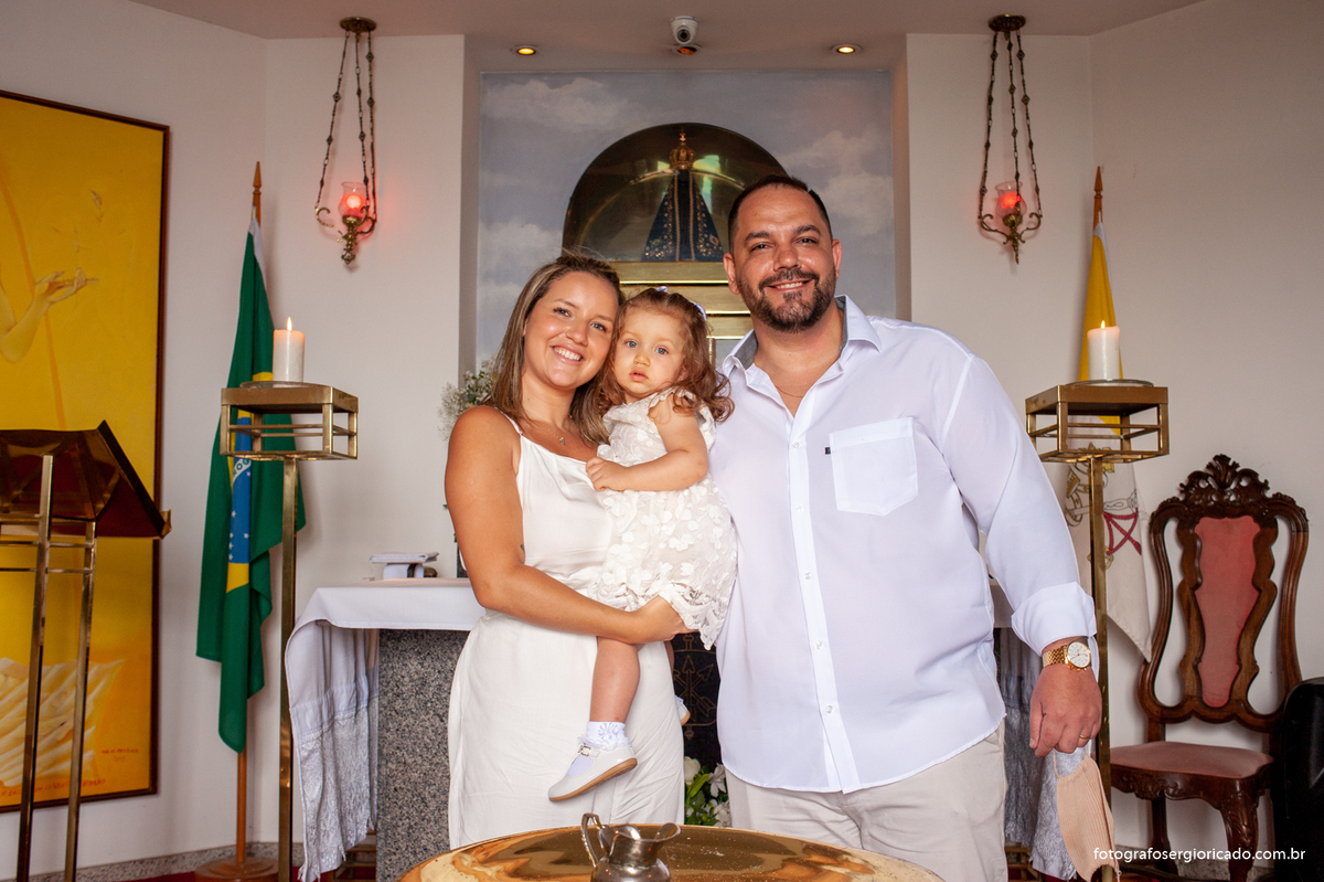 Fotografia dos pais com criança na cerimônia de batismo na Capela de Nossa Senhora Aparecida no Cristo Redentor localizado no Morro do Corcovado no Rio de Janeiro
