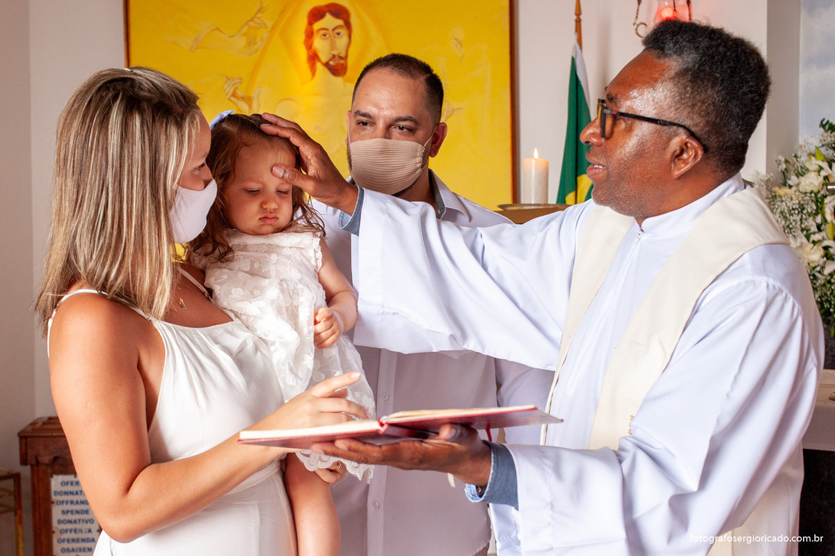 Foto dos pais com o padre realizando cerimônia de batismo na Capela de Nossa Senhora Aparecida no Cristo Redentor localizado no Morro do Corcovado no Rio de Janeiro