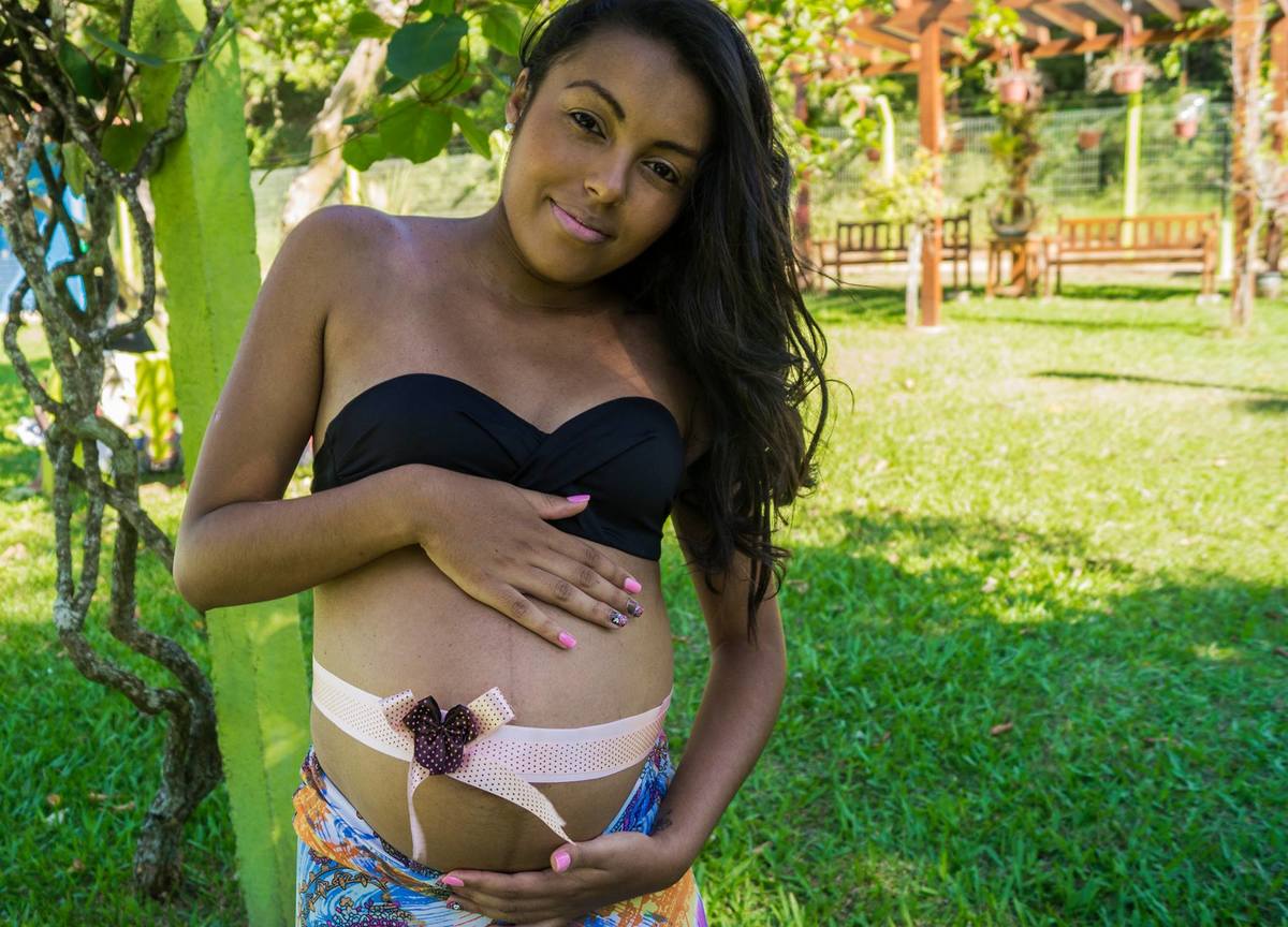 Em meio a natureza a mãe com um laço na barriga posa para a foto
