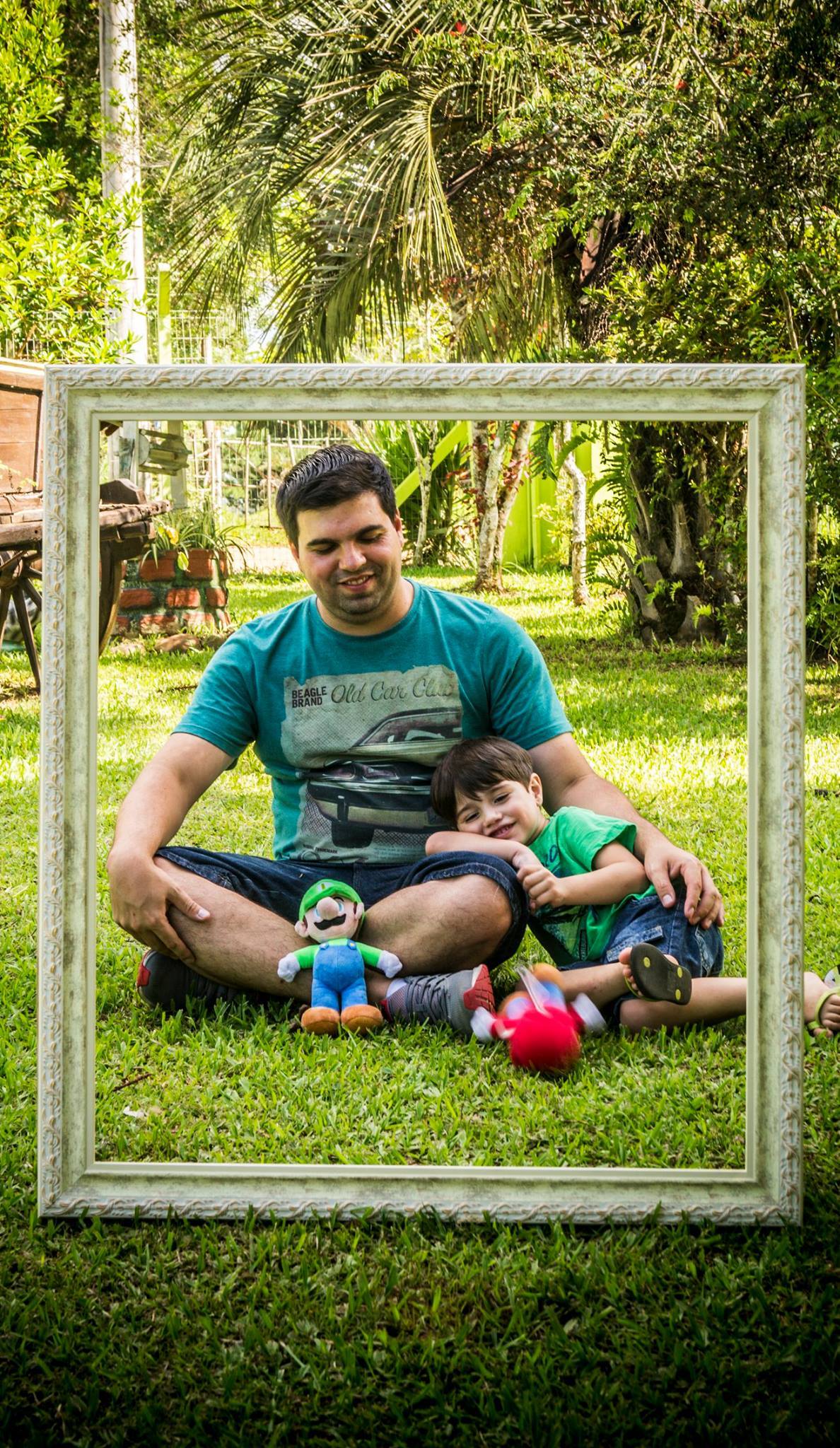 Pai e filho sentados na grama, filho se apoia na perna do pai