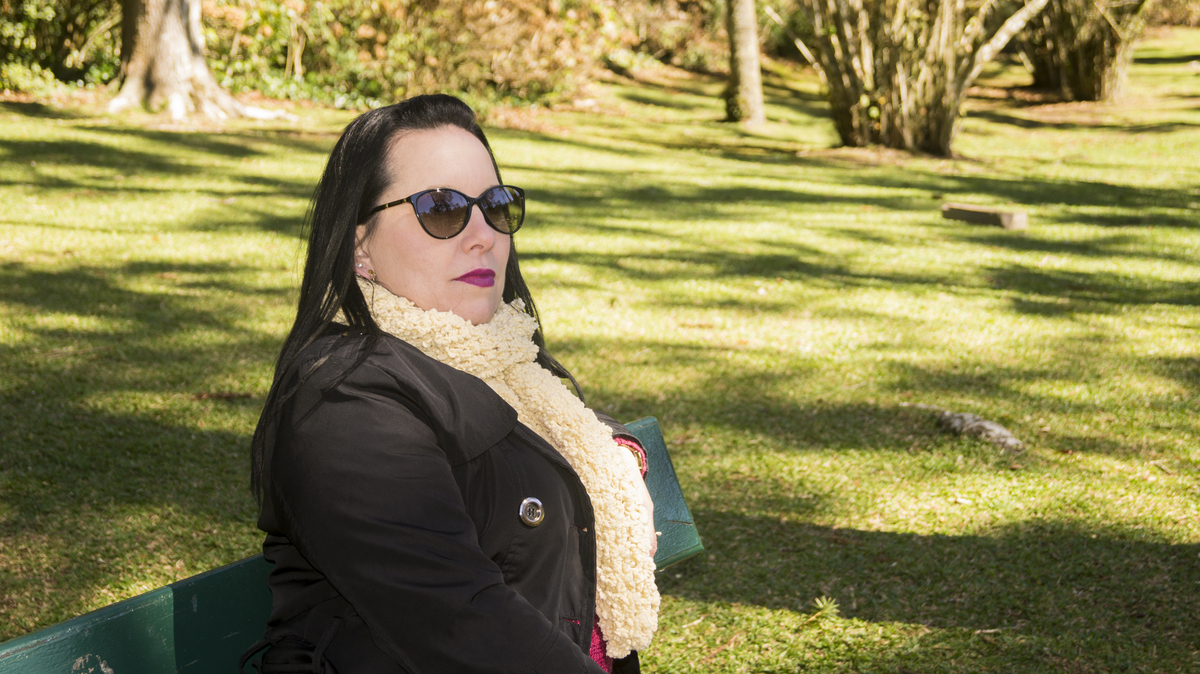 Foto da Tatiane sentada no banco em meio a natureza