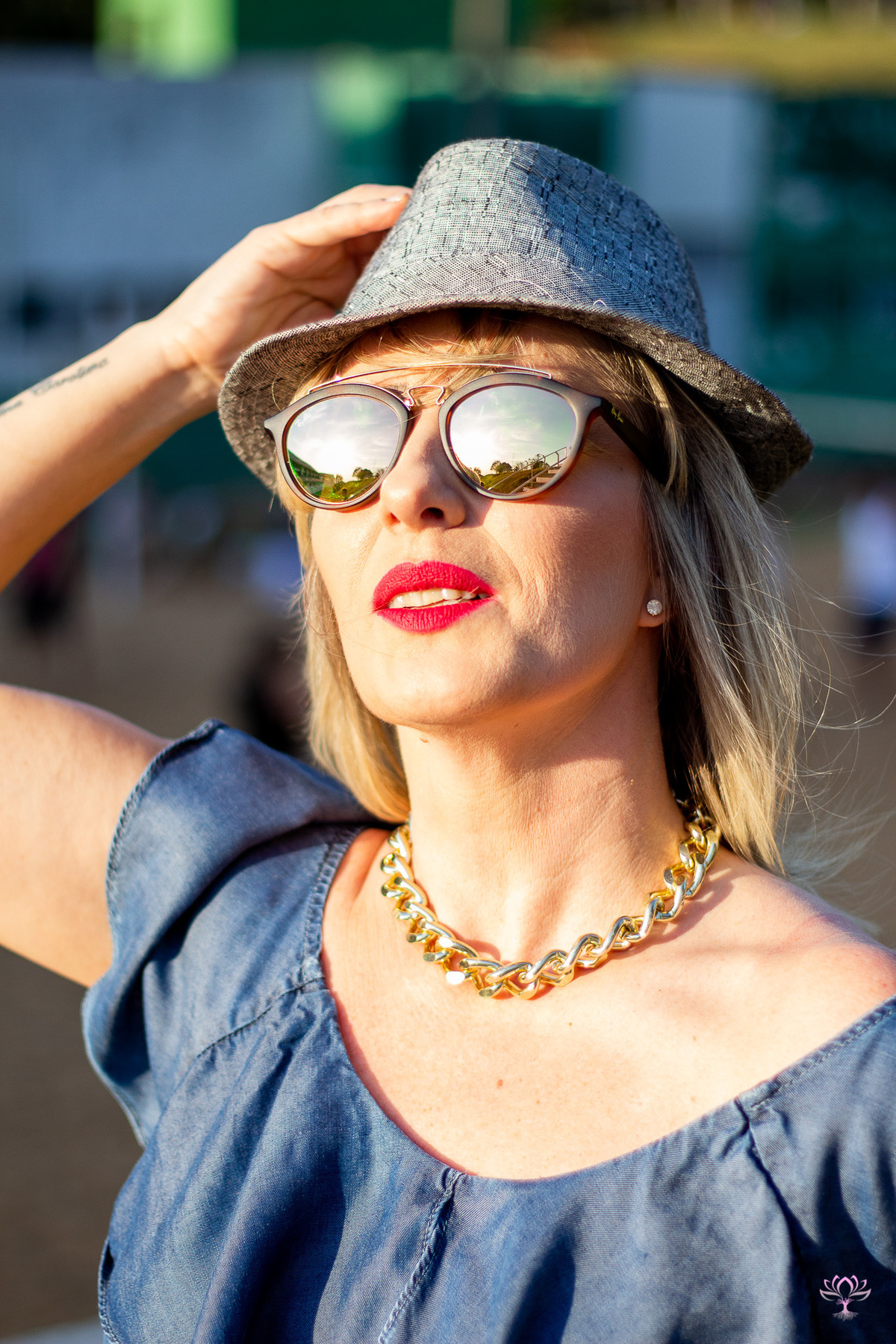 mulher segurando o chapéu na cabeça de óculos escuros