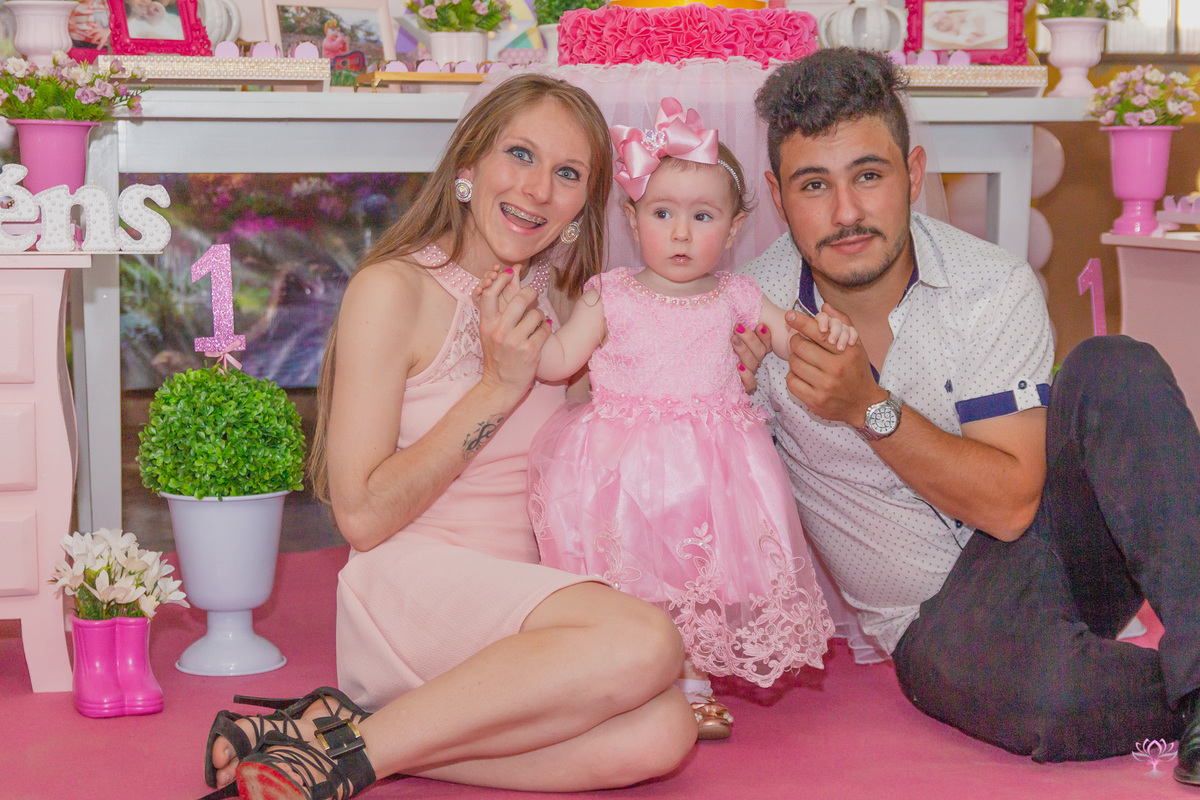 família sorrindo para foto na festa de 1 ano da filha.