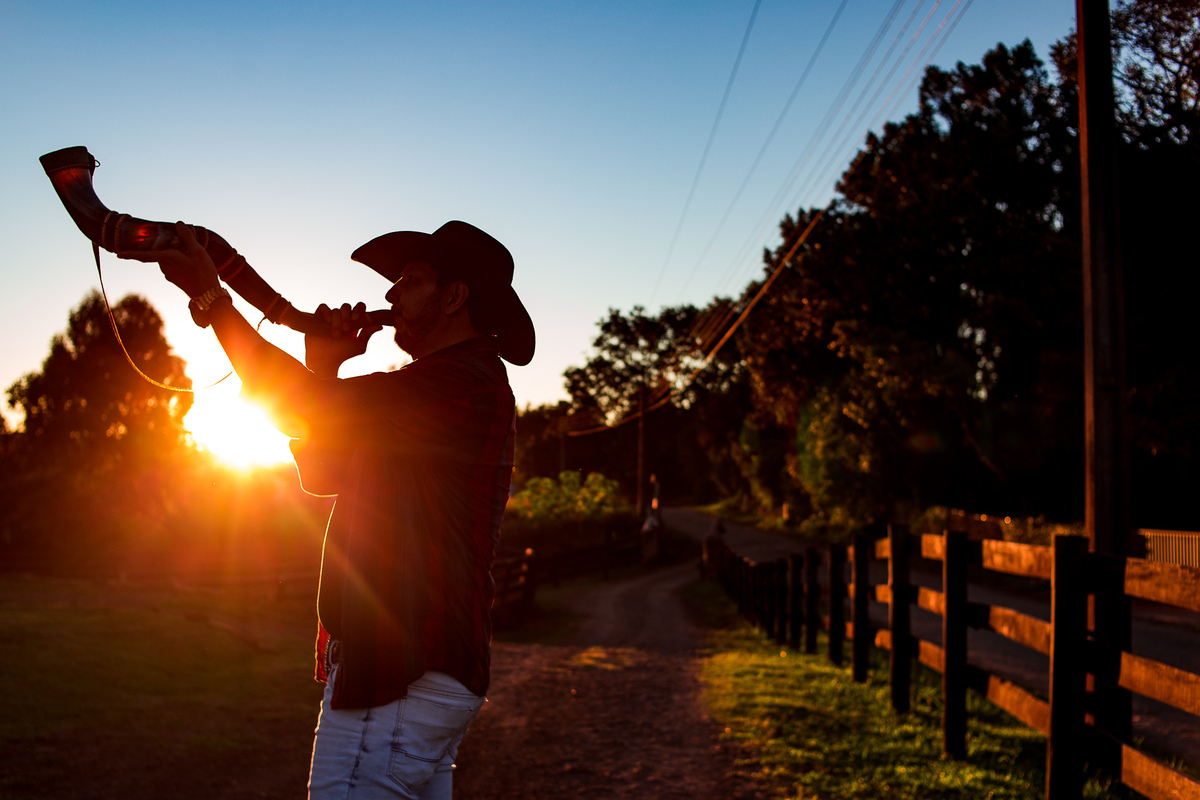 Homem tocando berrante com o sol ao fundo no fim do dia na Cabanha Baturitê em Chapecó
