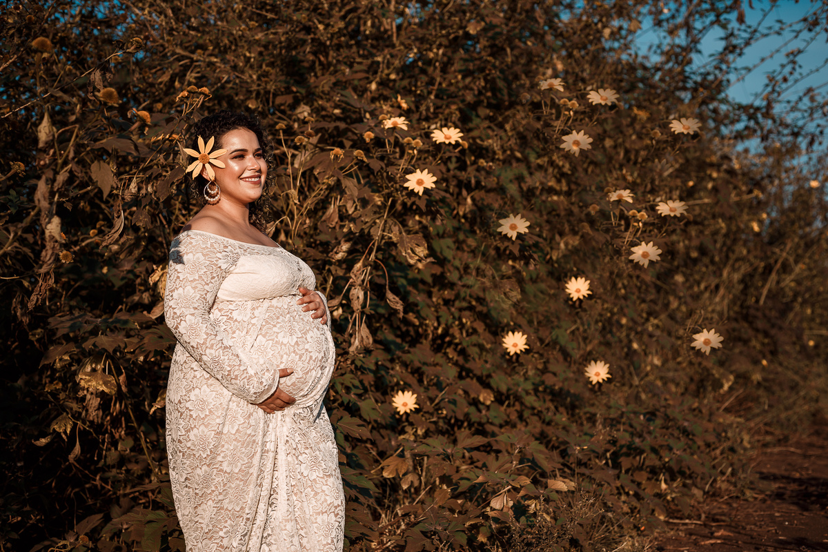 gestante com o rosto iluminado pelo sol em uma parede de flores amarelas