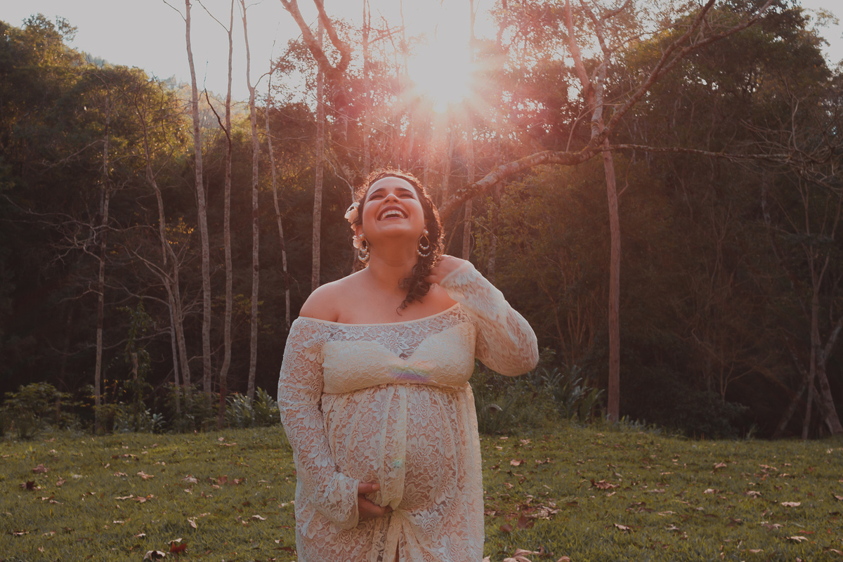 gravida gargalhando, sol estrelado ao fundo, grama com folhas secas
