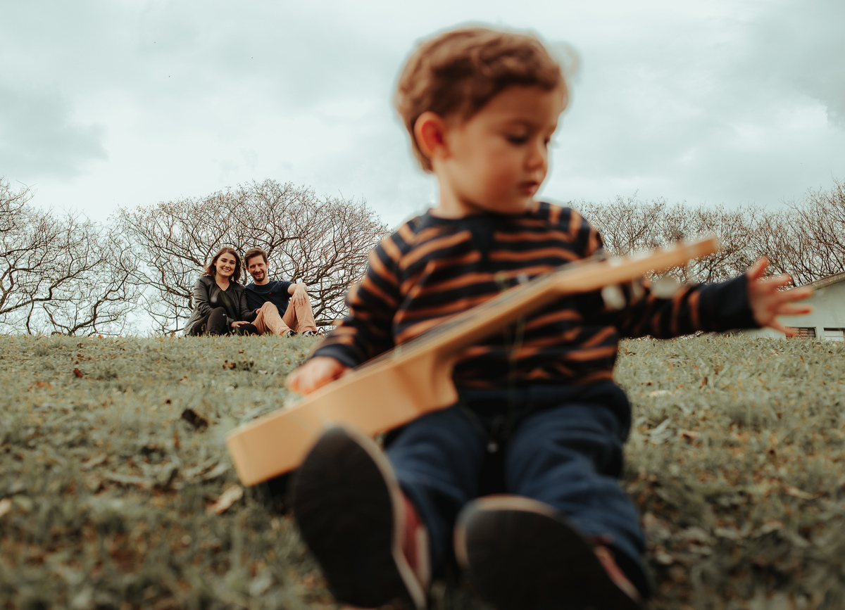 criança brincando com violão, pais ao fundo