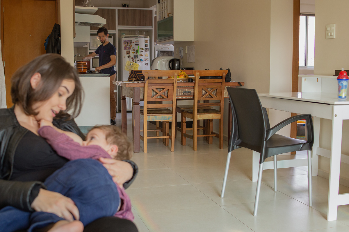 mãe amamentado e pai cozinhando ao fundo