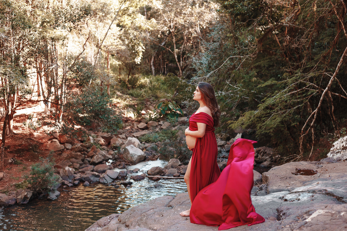 gestante de vestido vermelho em cima de uma pedra