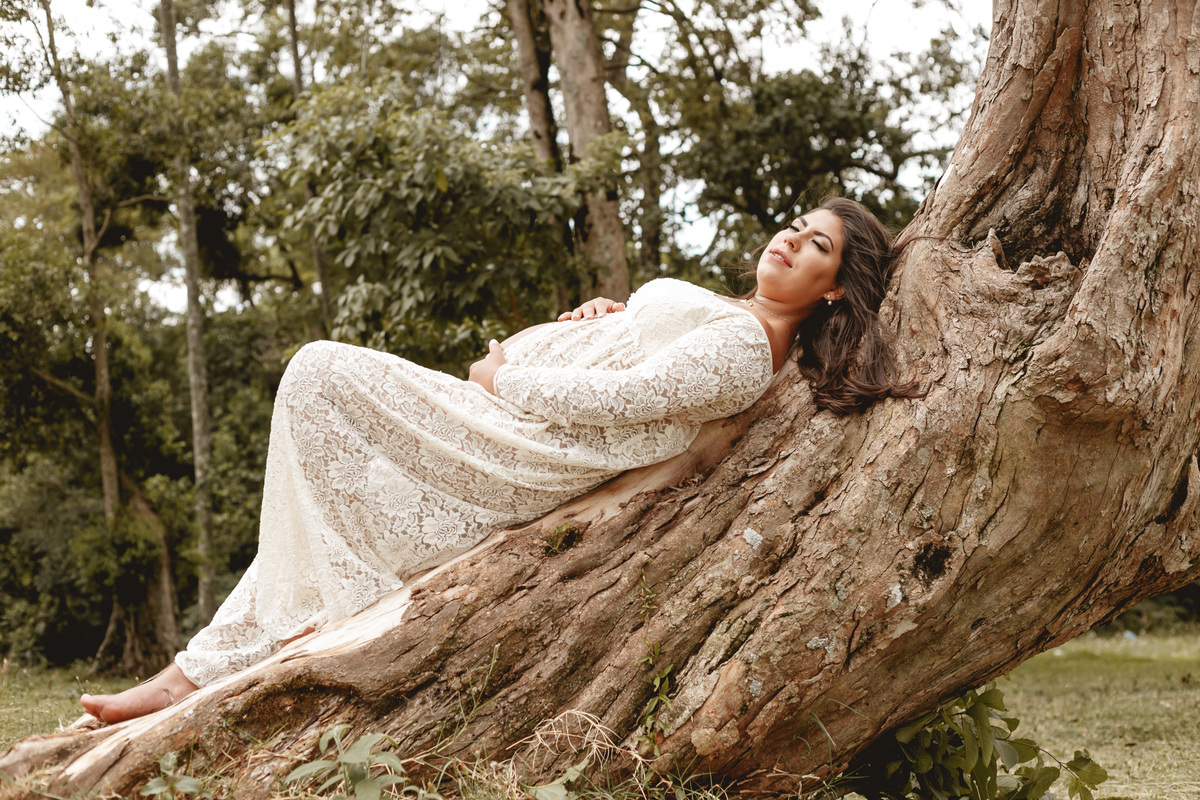 gestante deitada no tronco de uma árvore
