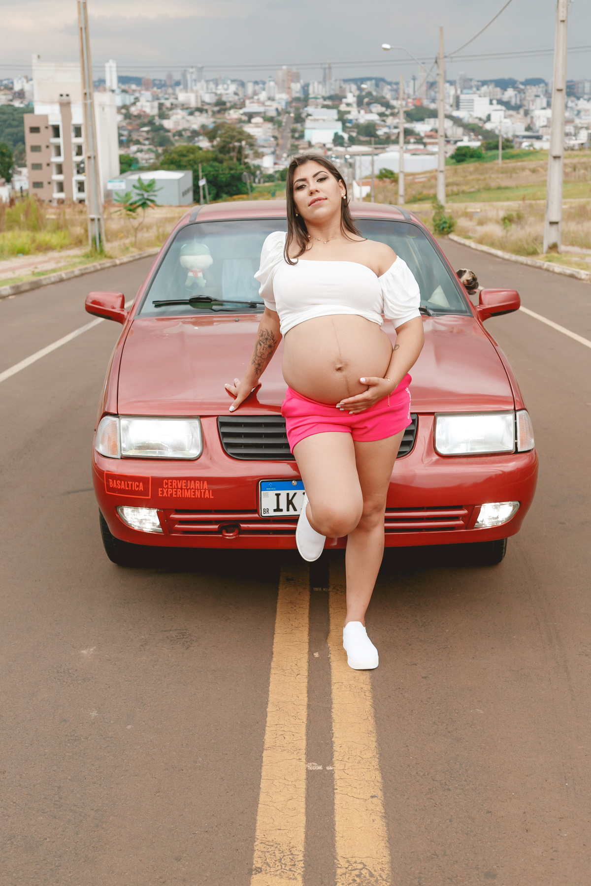 gestante posando na frente do carro, um santana vermelho