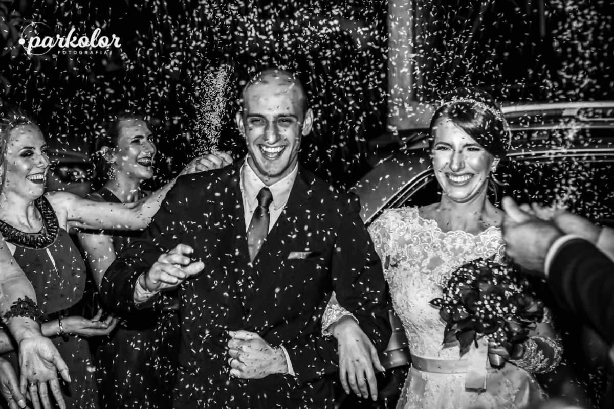 fotografia preto e branco Parkolor Gravataí RS, 
foto saída da igreja com arroz jogado nos noivos, padrinhos celebrando ao lado com muito amor, entrada do salão de festa do casamento, noiva com vestido elegante e longo, muito felez pra foto