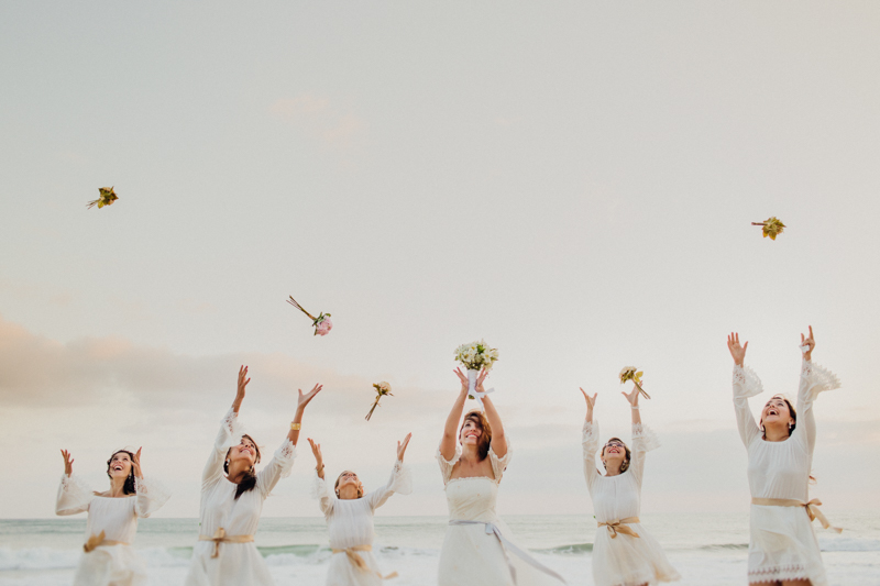 As madrinhas com a noiva, numa foto bem divertida. A noiva e as madrinhas são jogando o buquê, num lindo cenário num casamento na praia. Fotos por Moyra e Tiago, fotógrafos de casamento.