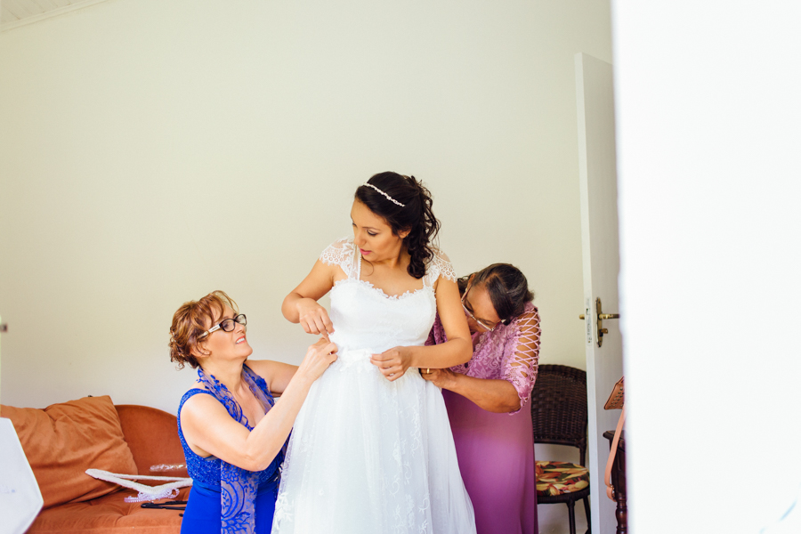 A noiva contou com a ajuda de sua mãe e sua sogra. Elas ajudaram a Paula a colocar seu vestido de noiva.