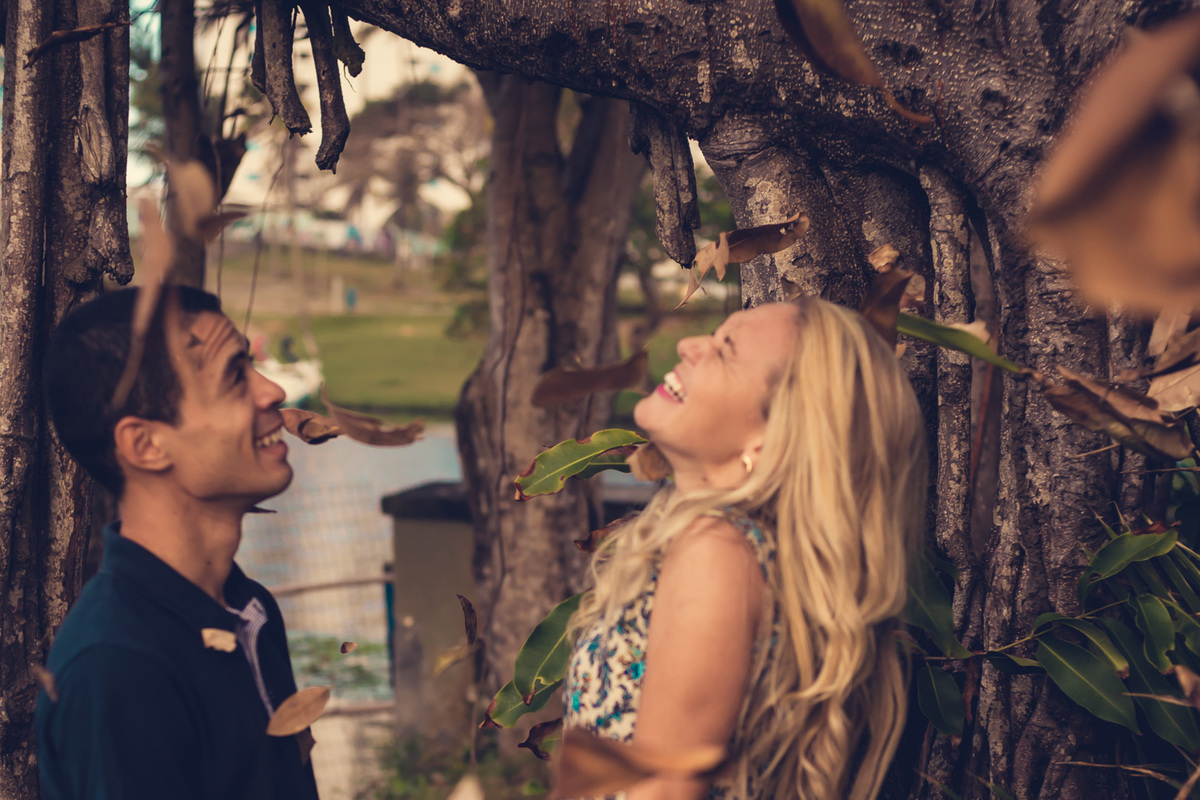 Fotografia de casal, ensaio pré-casamento, casal sorrindo com a chuva de folhas no Parque de Pituaçu, Salvador - BA