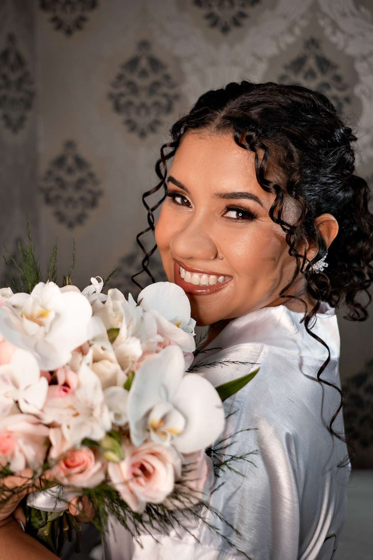 Momento de sorriso espontâneo da noiva de robe, retrato no making of antes do casamento no Salão do Reino.