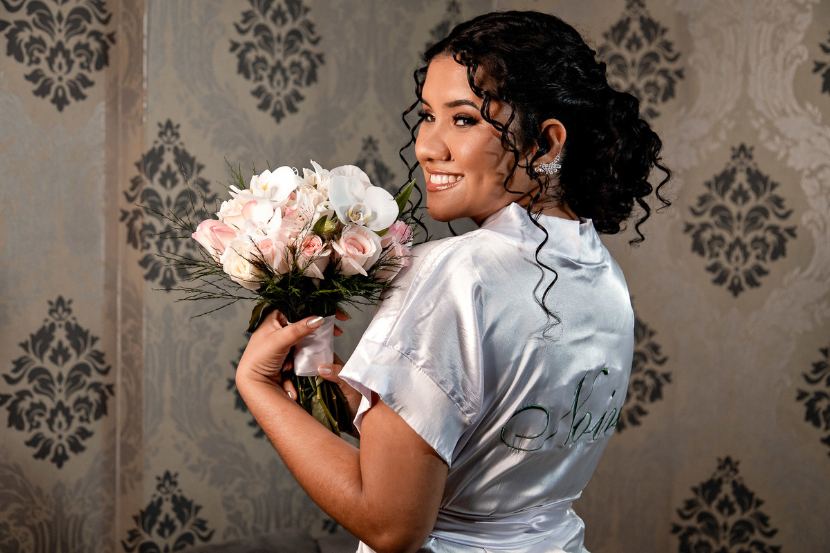 Noiva posando de robe perto da janela, luz natural valorizando o making off da noiva em Salvador – BA