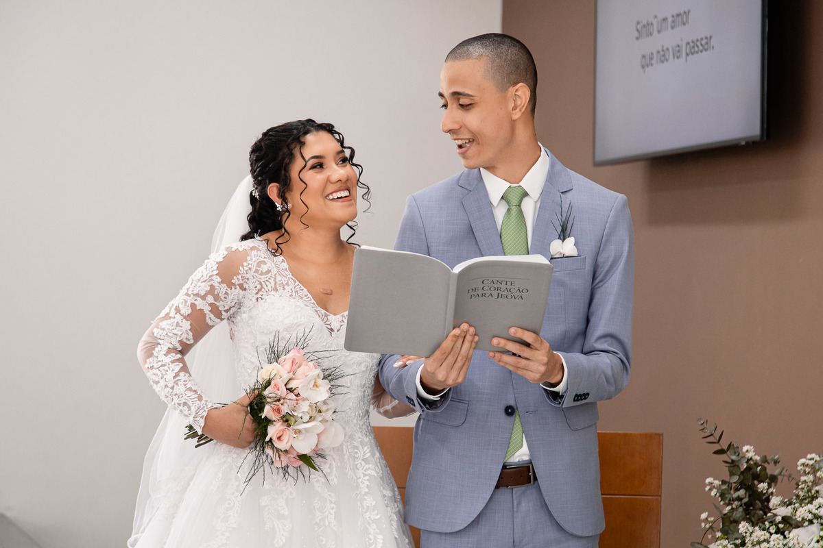 Noivos juntos cantando durante a cerimônia, momento especial no casamento no Salão do Reino.