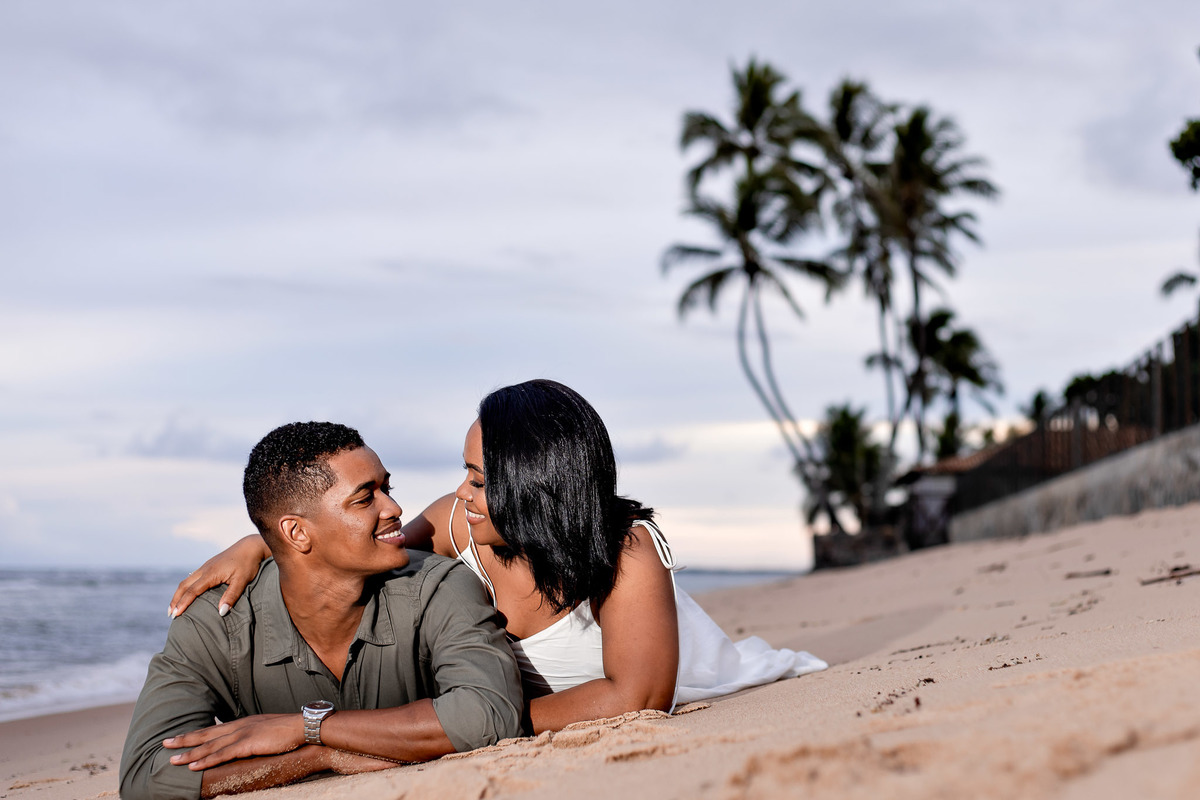 ensaio pré-casamento casal deitado areia Bahia, fotografia casal areia praia Salvador, ensaio pré-nupcial pose relaxada Praia do Forte, fotografo casamento pose areia Bahia, casal deitado praia fotografia romântica, ensaio noivos areia coqueiros Bahia, po