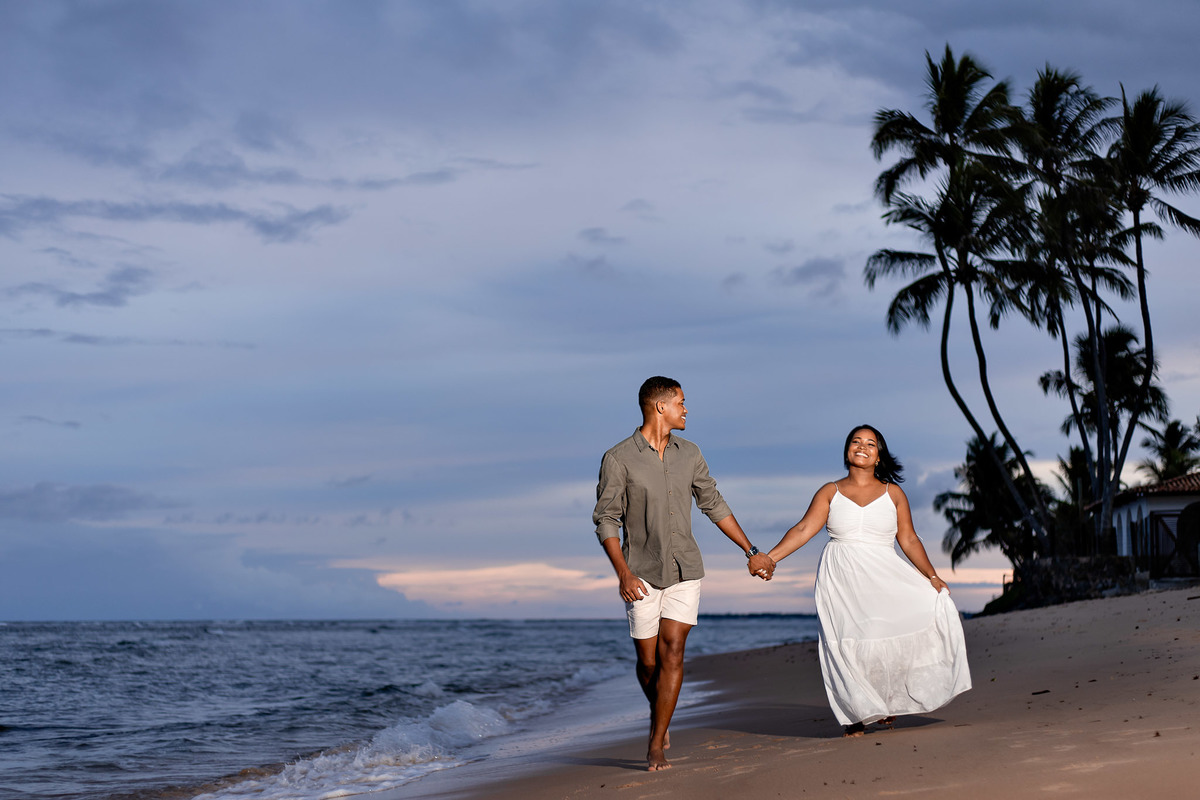 ensaio pré-casamento blue hour caminhando praia, fotografia casal blue hour Salvador Bahia, ensaio pré-nupcial crepúsculo Praia do Forte, fotografo casamento crepúsculo praia Bahia, casal caminhando anoitecer praia fotografia, ensaio noivos silhueta coque