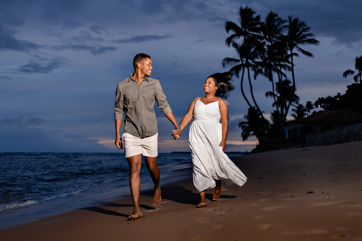 ensaio pré-casamento vestido vento anoitecer Bahia, fotografia casal anoitecer praia Salvador, ensaio pré-nupcial movimento vestido Praia do Forte, fotografo casamento movimento natural noite Bahia, vestido branco vento ensaio praia noivos, ensaio casal a