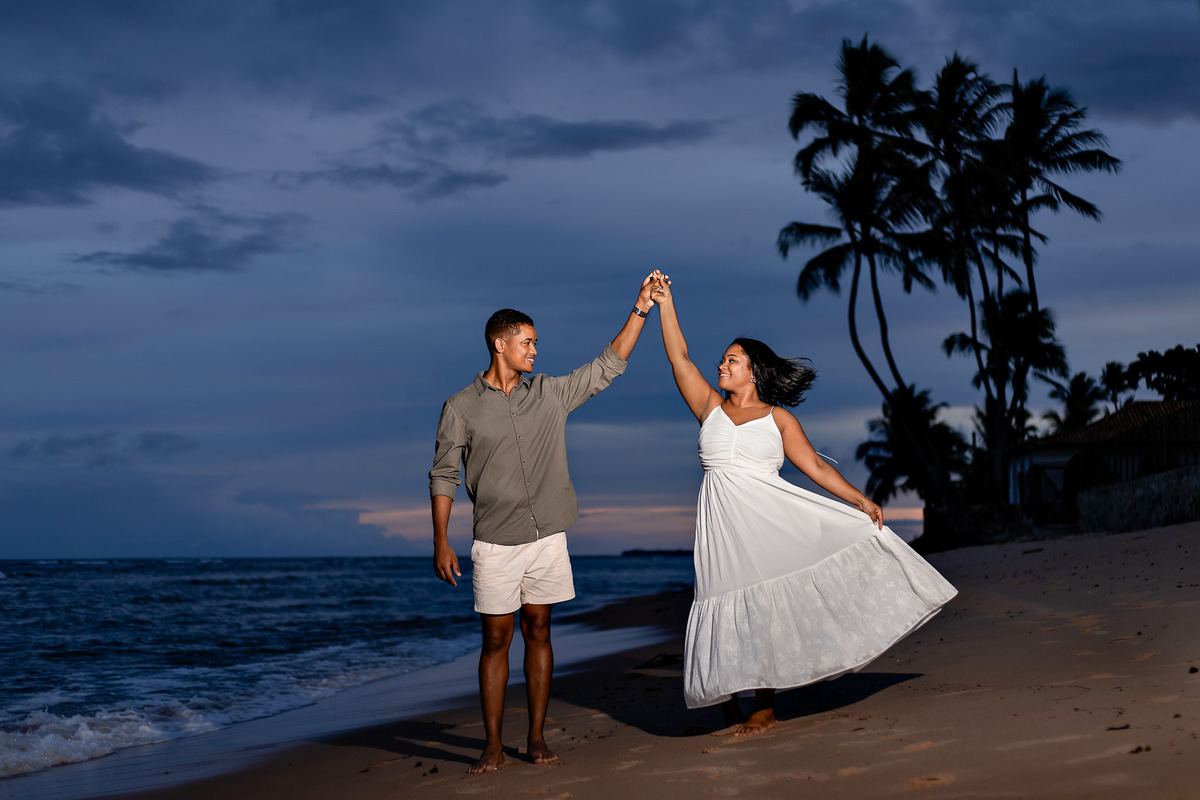 ensaio pré-casamento blue hour Praia do Forte, fotografia noturna casal praia Bahia, ensaio pré-nupcial anoitecer Salvador, fotógrafo casamento flash noite Bahia, casal dançando praia anoitecer Bahia, ensaio noivos luz noturna Praia do Forte, fotografia d