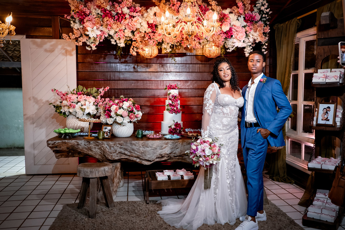 Noivos ao lado da mesa de doces decorada com flores na festa de casamento em Salvador