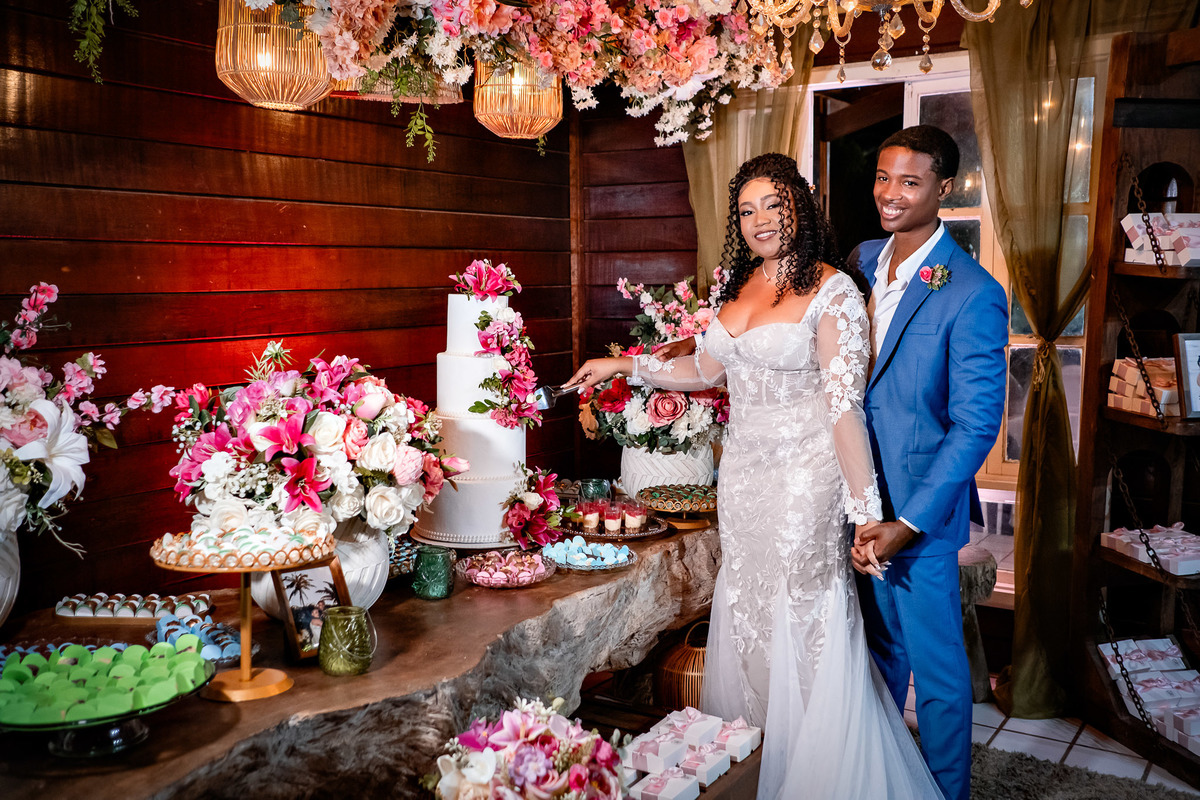 Noivos ao lado do bolo decorado com flores na festa de casamento em Salvador