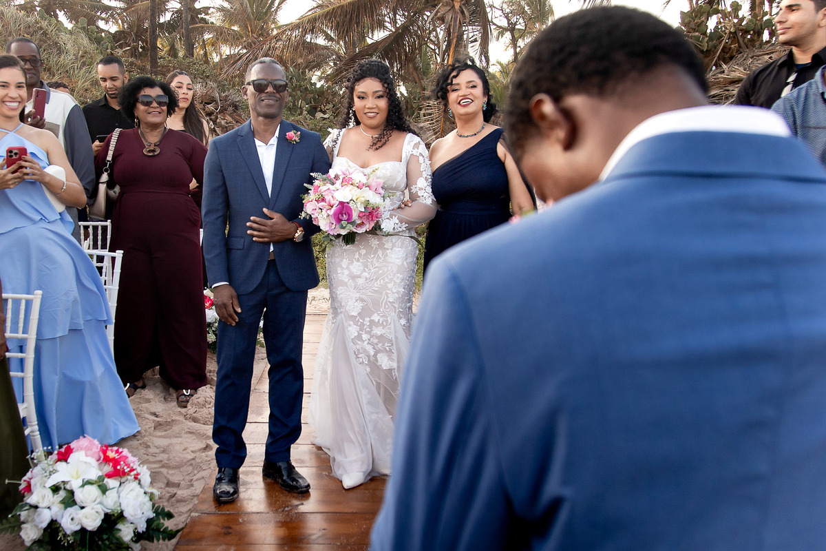 Noiva com o buquê ao lado do cortejo durante casamento na praia em Salvador