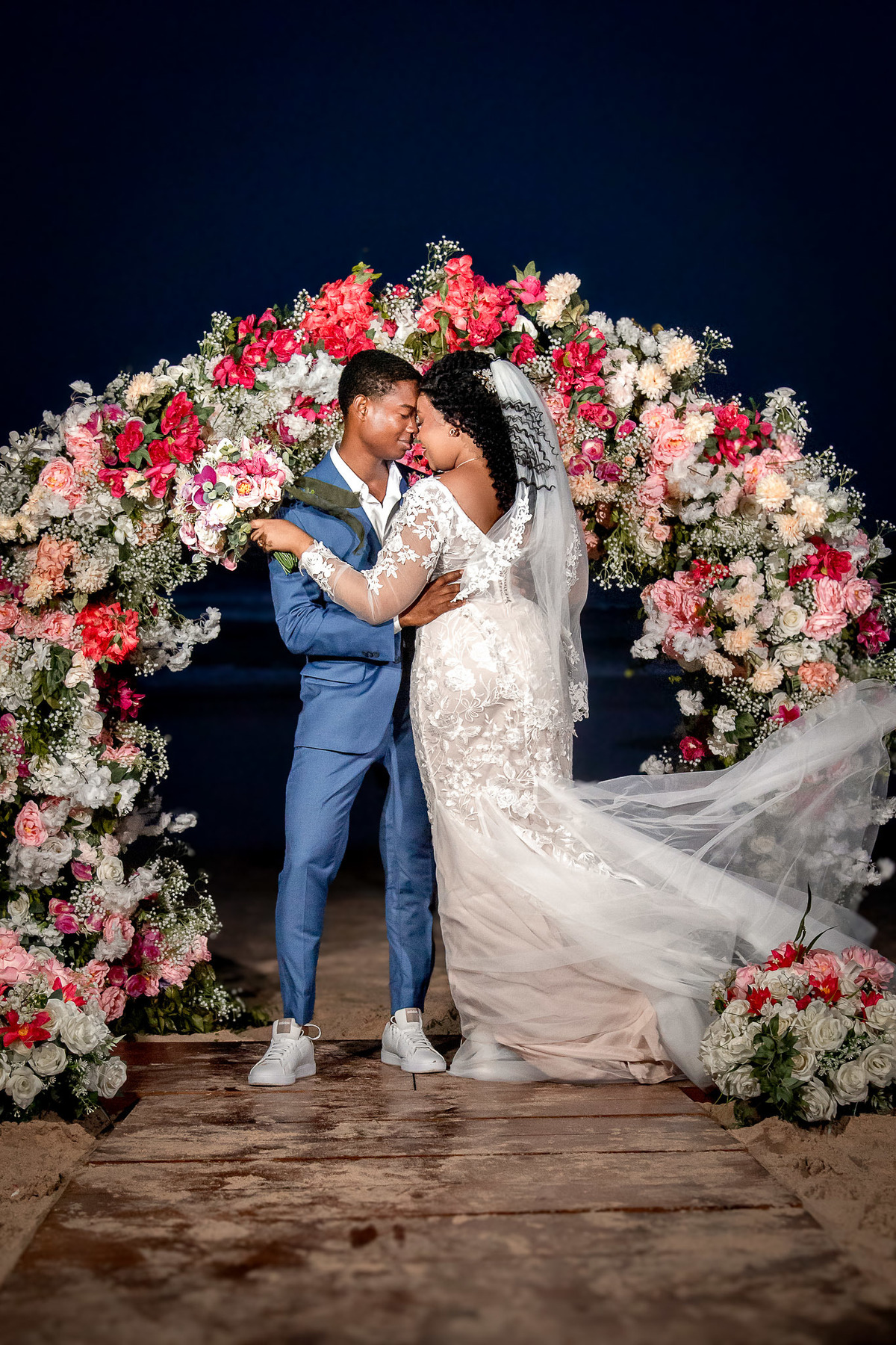 Noivos se beijando sob arco de flores durante a festa de casamento em Salvador