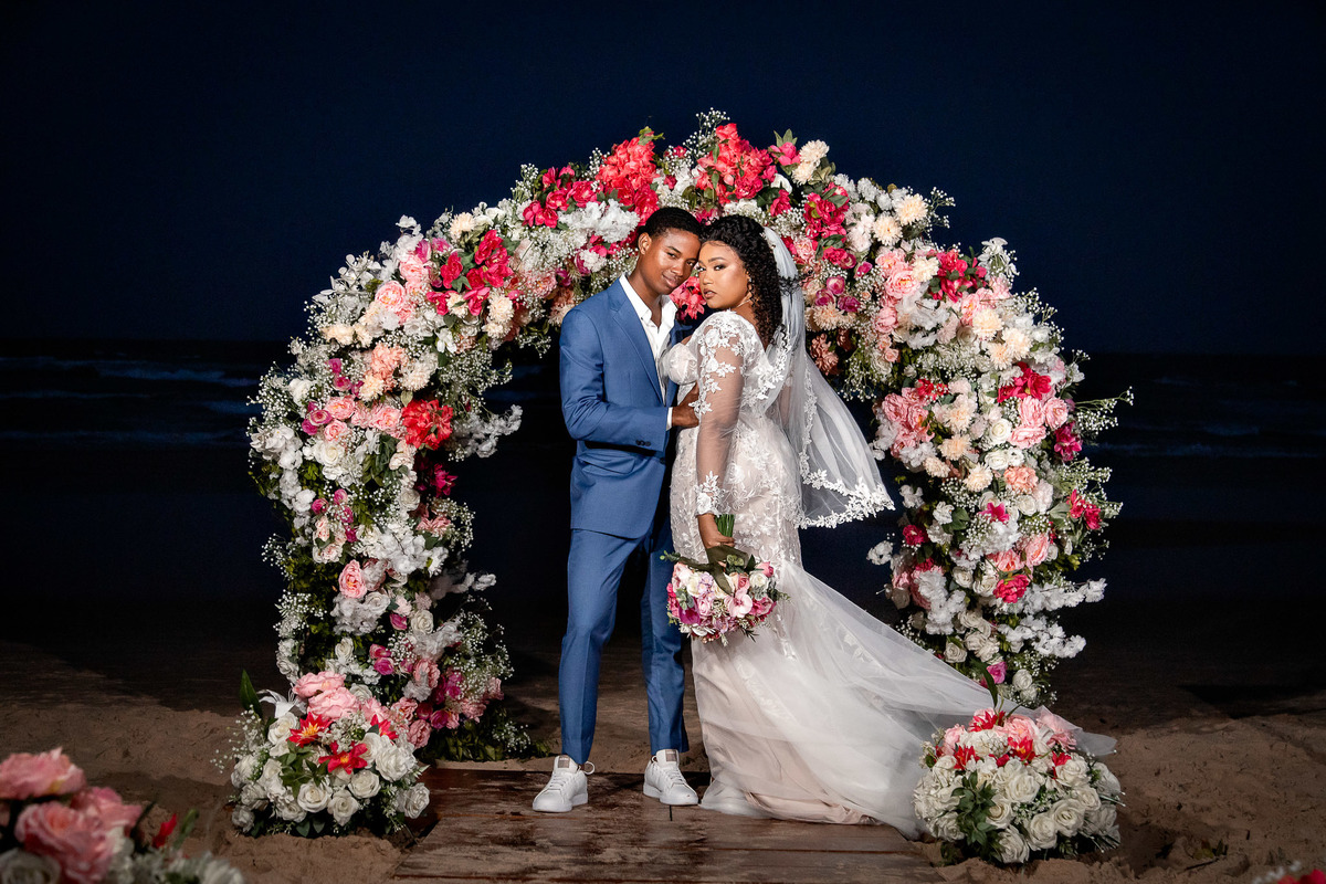 Noivos posando juntos sob o arco de flores durante a festa de casamento em Salvador