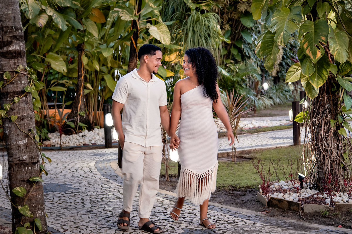 Casal caminhando ao entardecer no jardim iluminado, ensaio pré-casamento na Praia do Forte