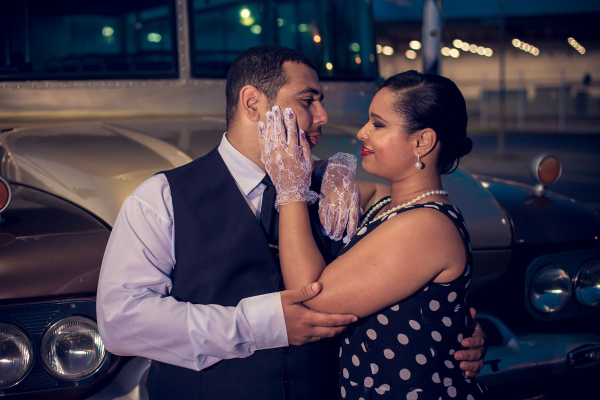 noiva alisando noivo com luva branca em estacionamento em frente a um carro antigo estilo anos 80 em Salvador