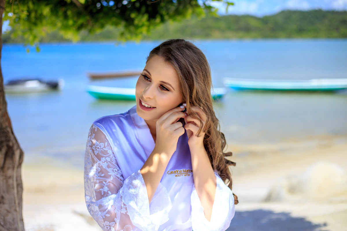 fotografia de noiva colocando o brinco com hobby de noiva na praia de Madre de Deus - Bahia 