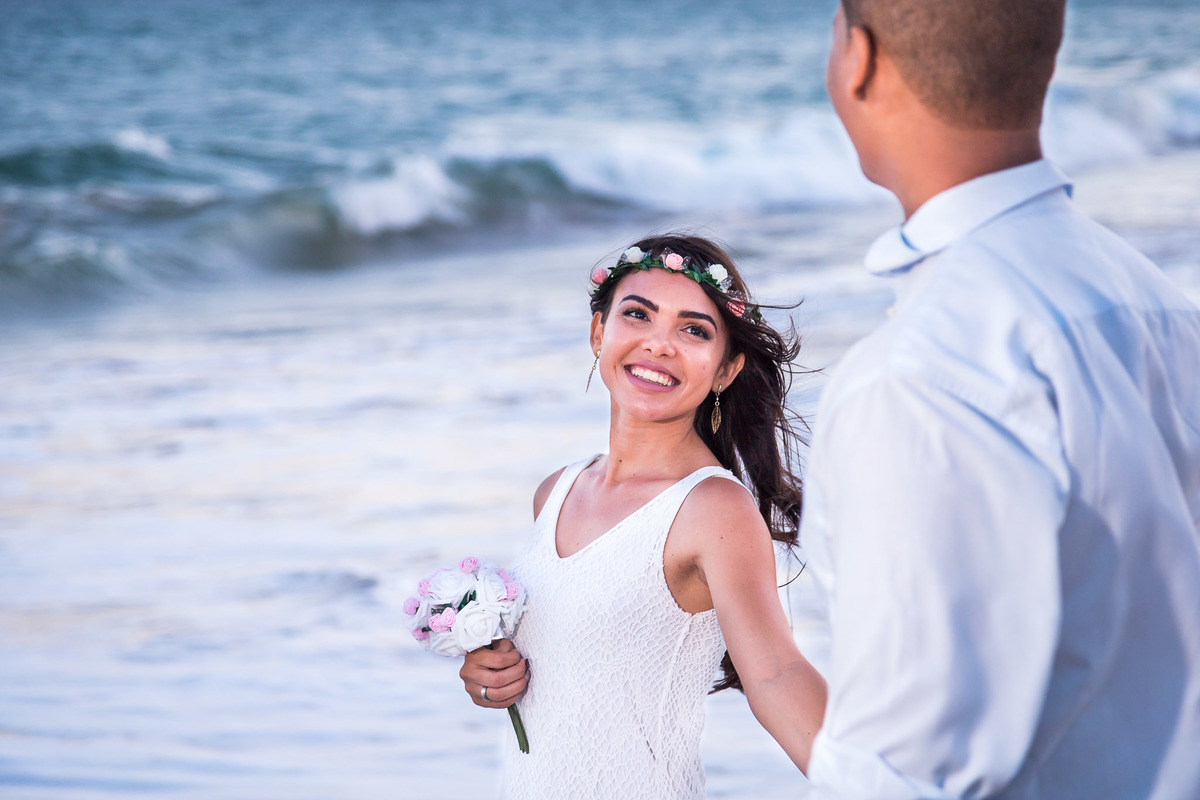 fotografia de noiva olhando para noivo na praia de Guarajuba correndo com cabelos ao vento