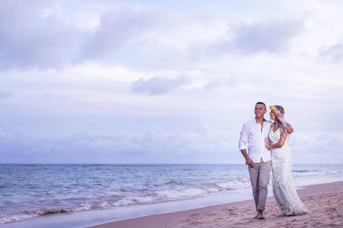 noivos com roupa branca na praia de Guarajuba olhando para o mar