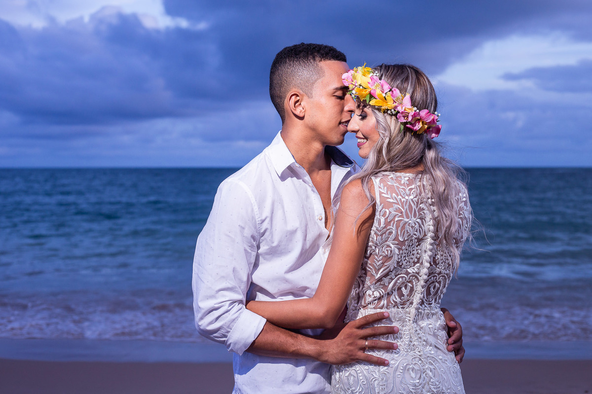 Fotografia de casal em ensaio pré-casamento com noiva usando coroa de flores naturais rosa na praia de Guarajuba