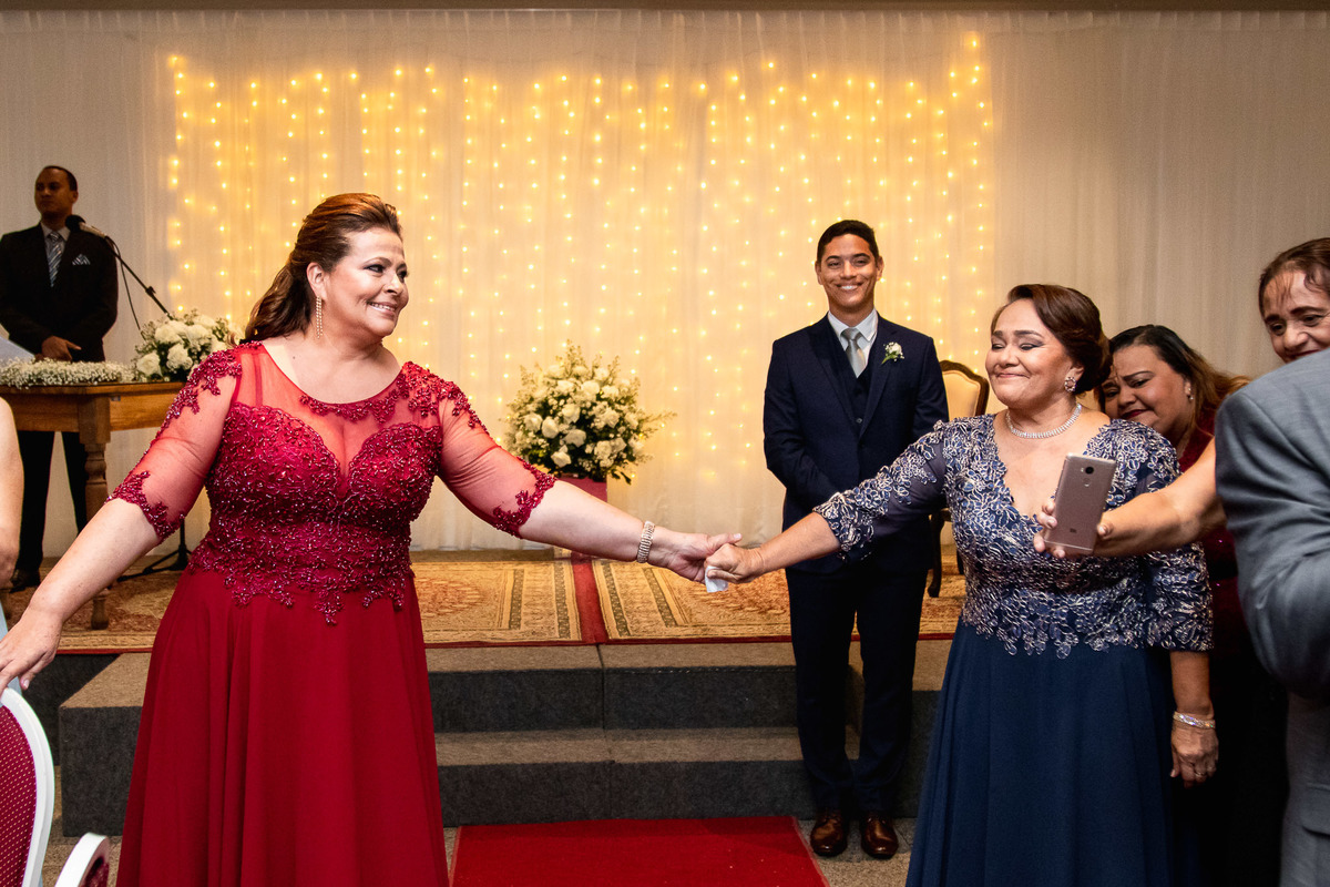 mães dos noivos se olhando sorrindo e noivo sorrindo na entrada da noiva