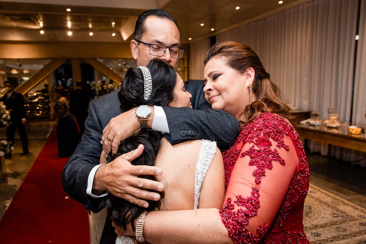 pais da noiva abraçando a noiva no casamento