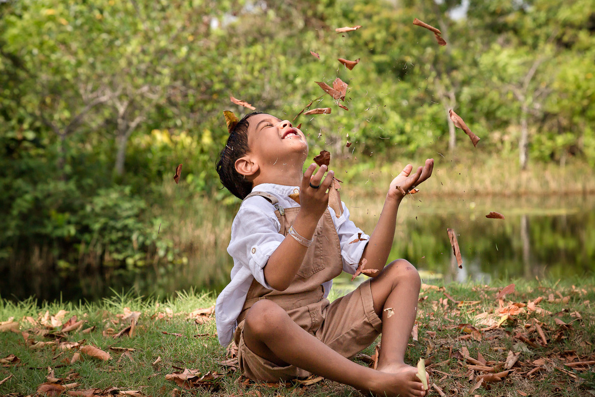 menino pequeno se divertindo com as folhas em um ensaio fotográfico no resort costa do sauipe