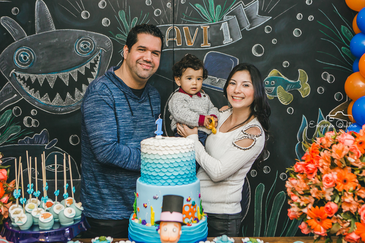 Aniversariante com seus pais na mesa do bolo brincando com a decoração Mundo Bita