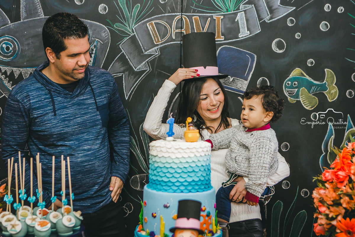 Aniversariante no colo da mãe ao lado de seu pai na mesa do bolo com decoração Mundo Bita