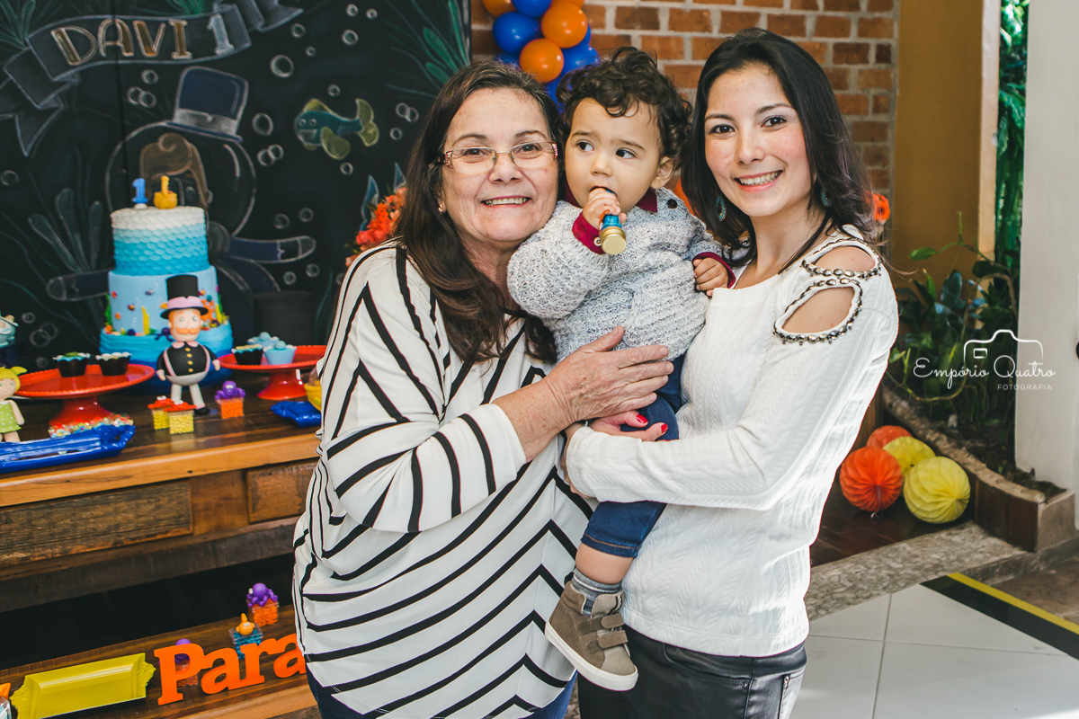 Aniversariante com sua mãe e avó em frente a mesa do bolo com decoração Mundo Bita