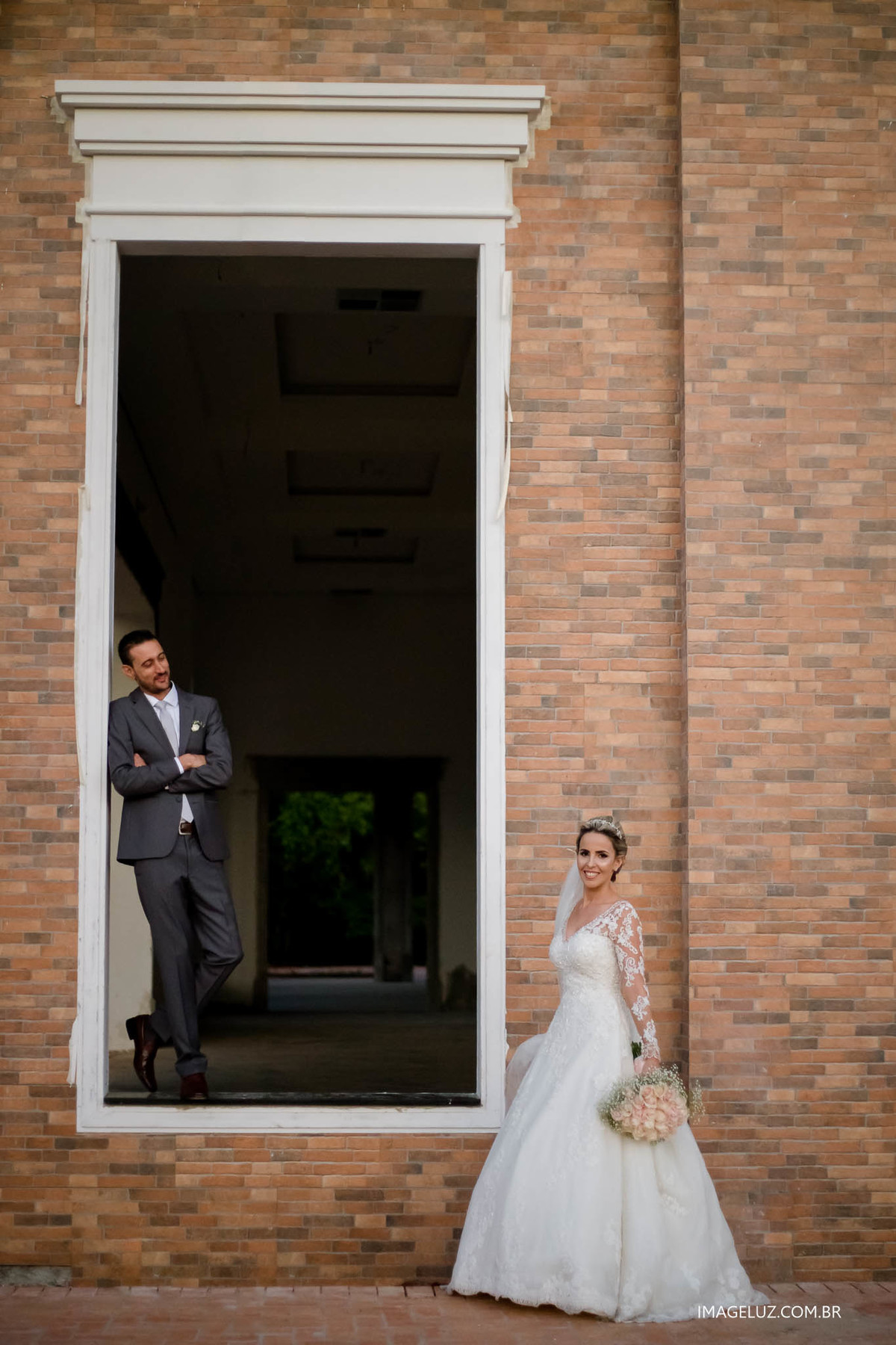 Foto incrivél do casamento da Fernanda e do Marcelo, noivos emoldurados por uma janela.